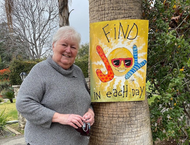 Member standing next to a palm tree with a positivity poster she designed pinned to it.