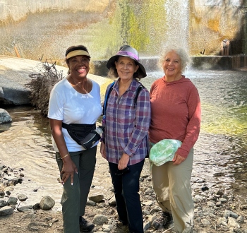 Three women standing in front of a river bank.