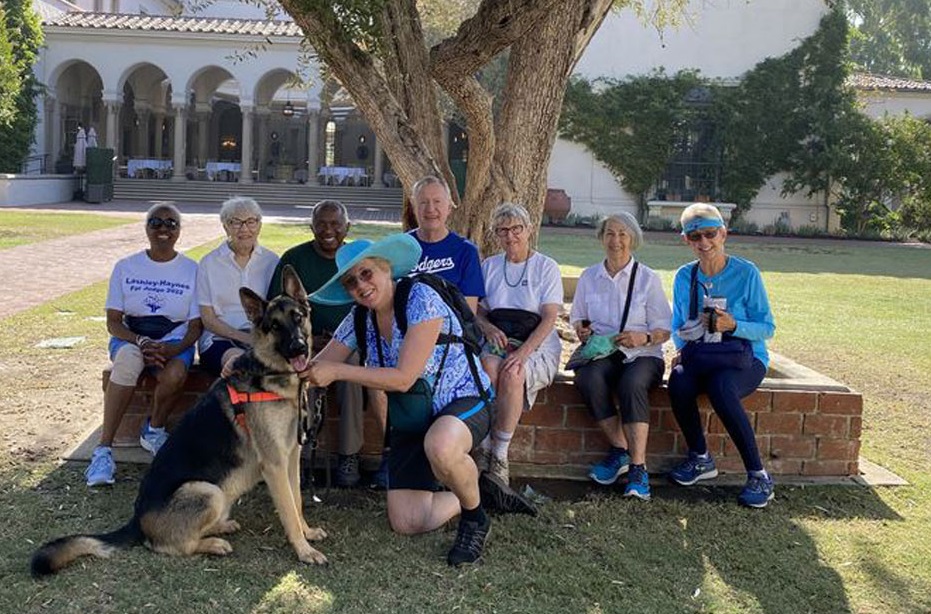 Eight people and a German shepherd, sitting underneath a tree in front of a historic building.