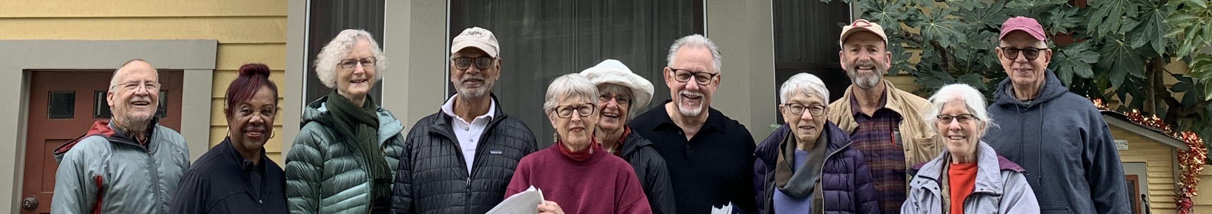 a group of older adults standing outside a yellow house