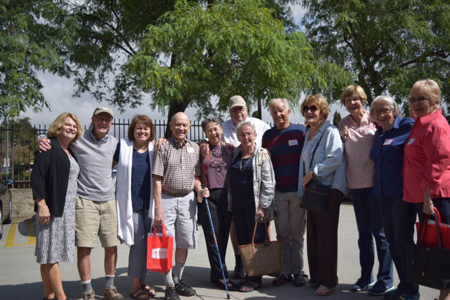 a group of older adults smiling for the camera with a fence and trees in the background