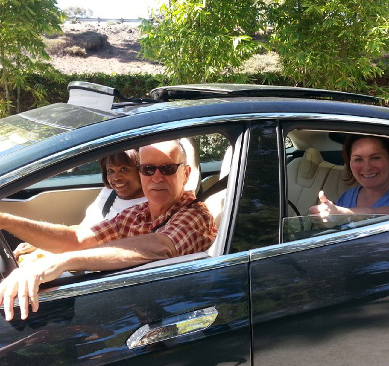 Three individuals in a car, the person in the backseat is giving a thumbs up.