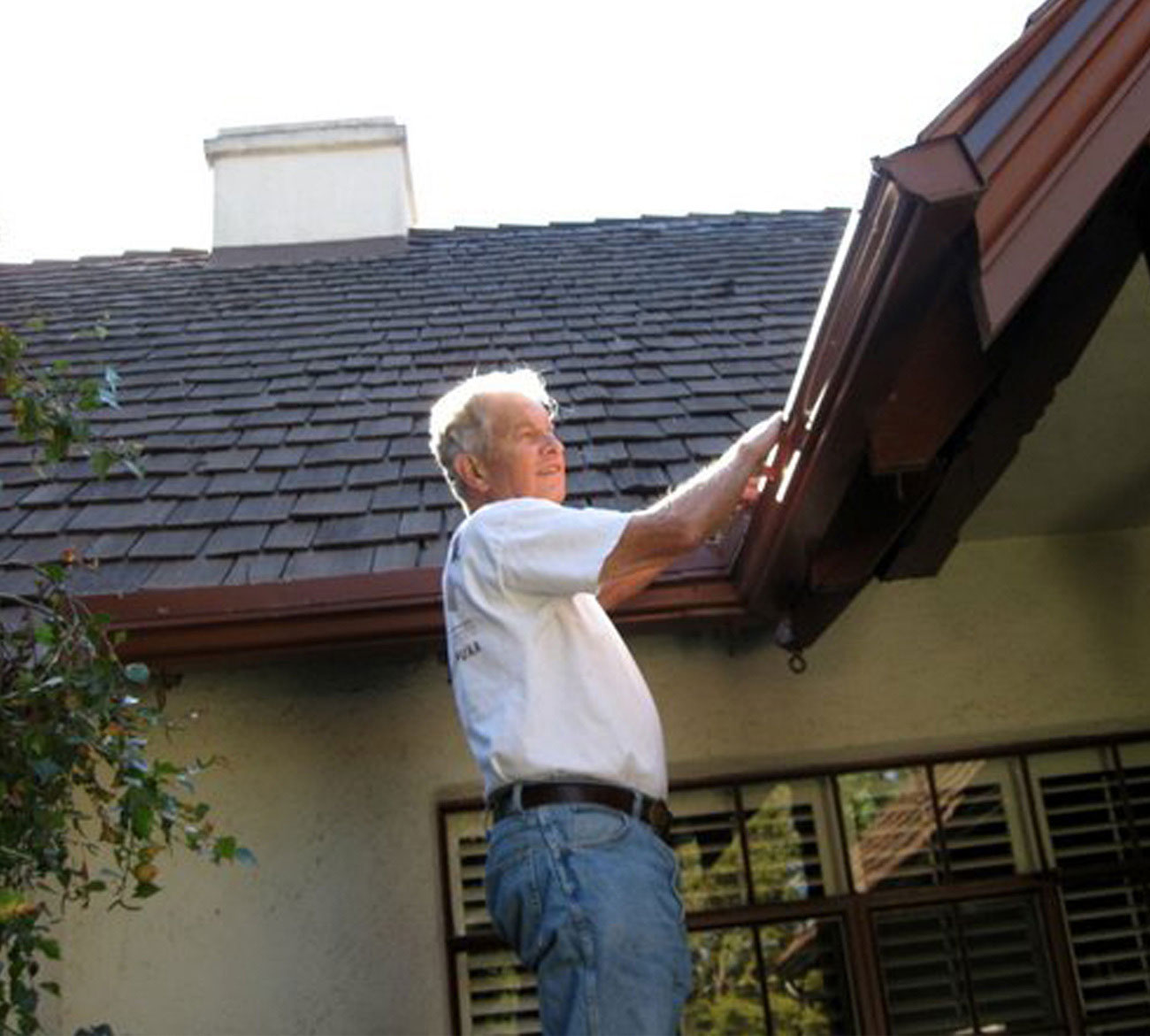 Man doing gutter maintenance, standing on ladder in front of house