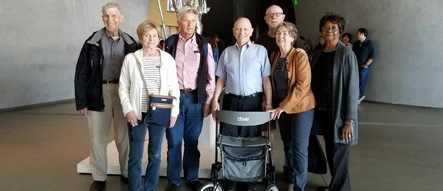 Seven older adults at in indoor art exhibit; one of the individuals has a walker.