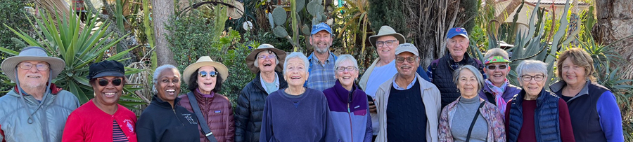 a group of older adults smiling with a bunch of different cactuses in the background