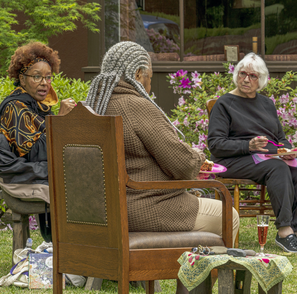 three older women sitting in chairs outside in a backyard garden